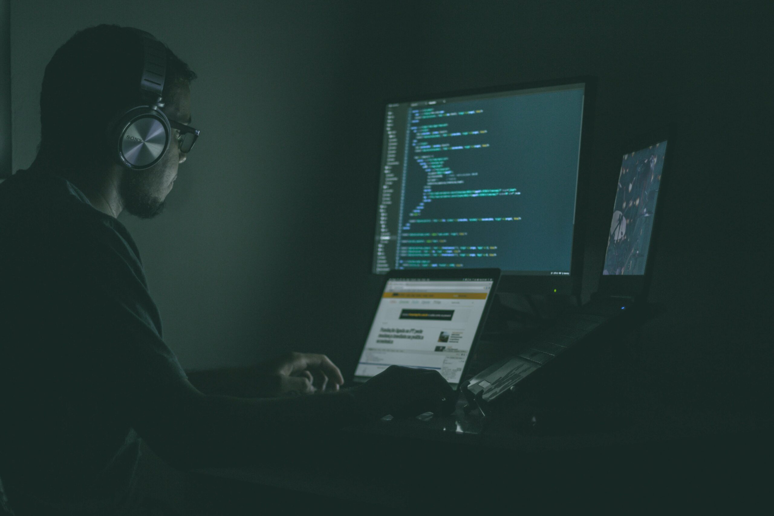 A guy coding on his computer in a dark room