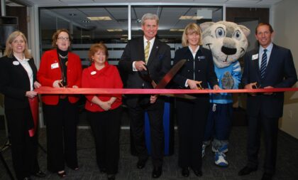 A group of Northwood University alum from the Grand Rapids chapter posing for a photo while cutting a red ribbon