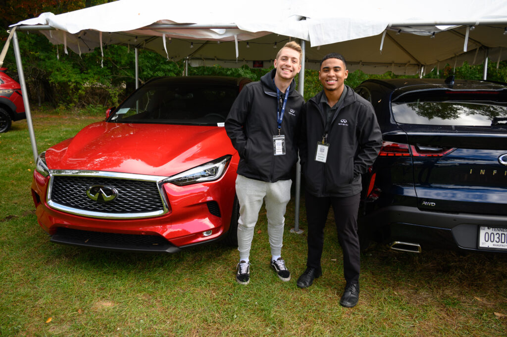 Two students pictured at Auto Show with a red car behind them