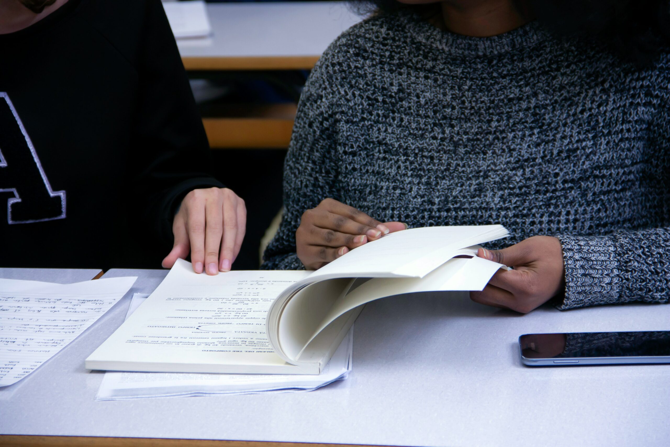 Two adult students flipping through a notebook