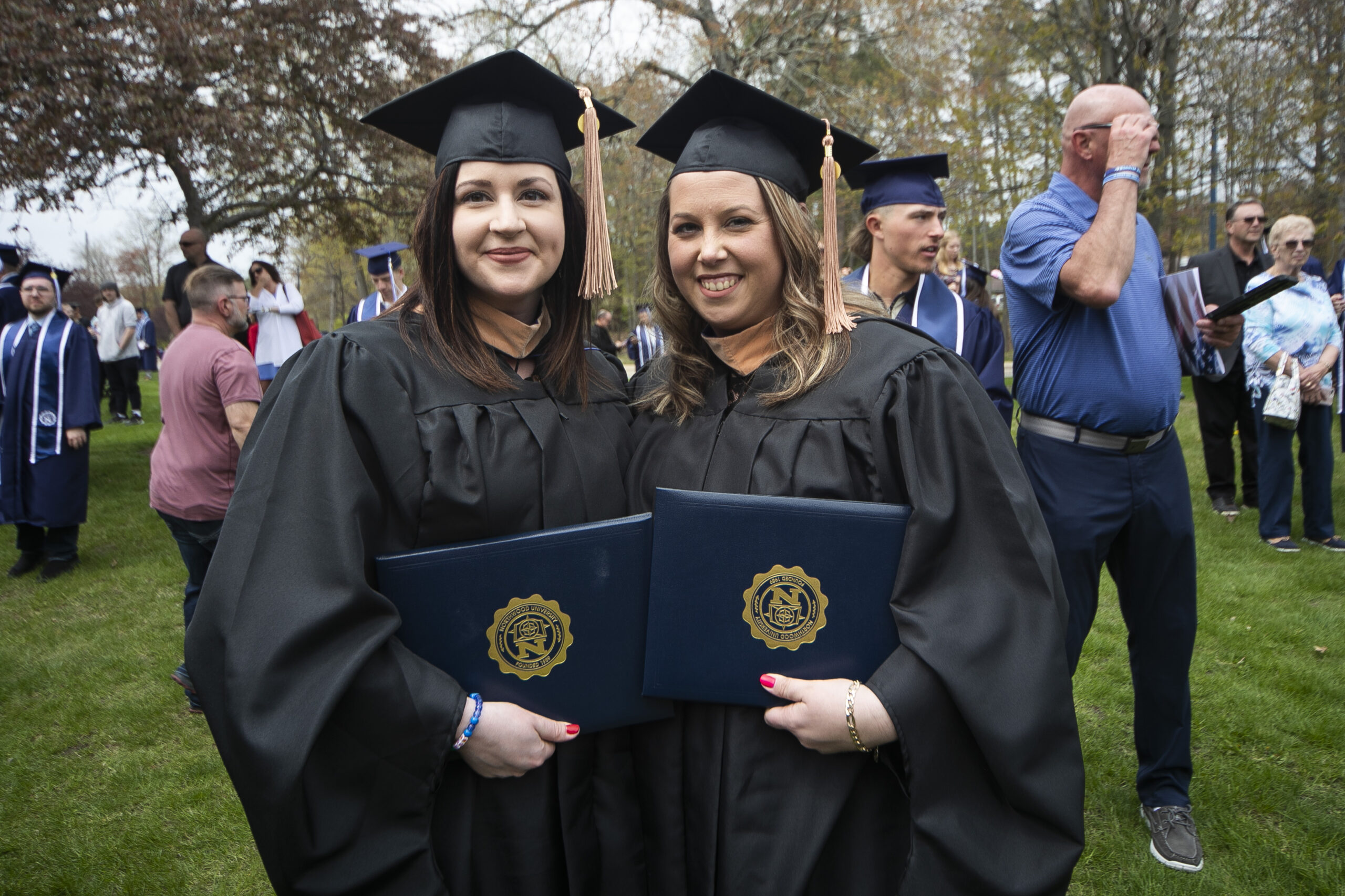 Two Northwood graduates in cap and gown holding up their diplomas outside