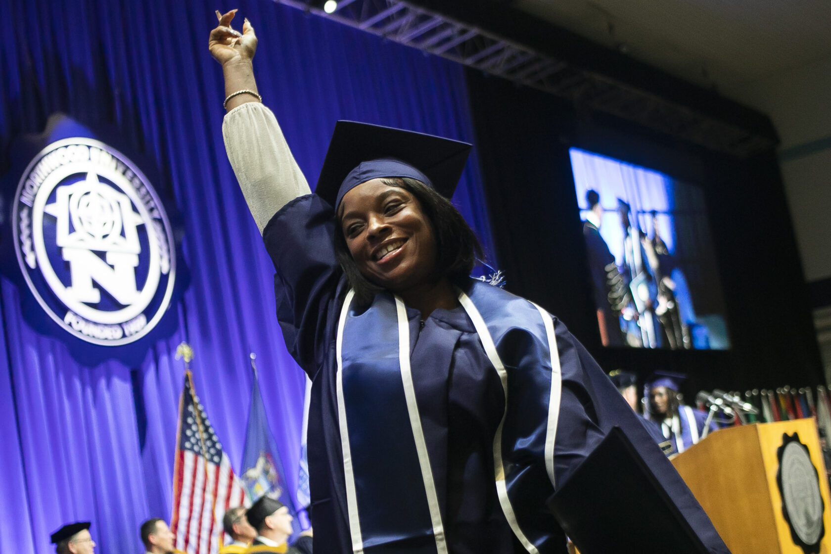 Northwood graduate holding a fist in the air, smiling, while walking off stage with her diploma.